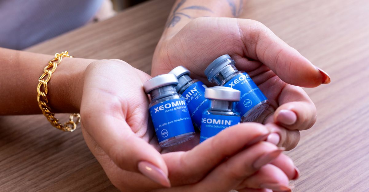 Female hands cradle Xeomin botulinum toxin bottles on a wooden table.